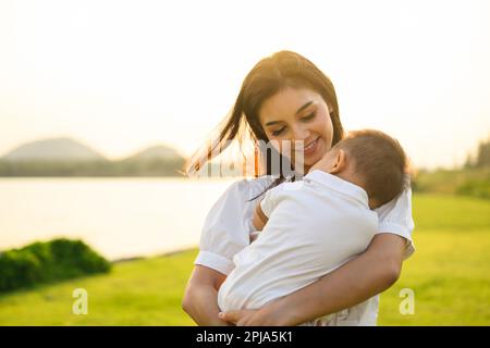 Liebevolle Mutter hält und trägt ihr Neugeborenes in einem öffentlichen Park Stockfoto