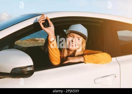 Die Frau, die mit dem Mietwagen fährt und die Schlüssel in einem offenen Fenster zeigt. Das Transportversicherungskonzept für Reiseurlaube Stockfoto