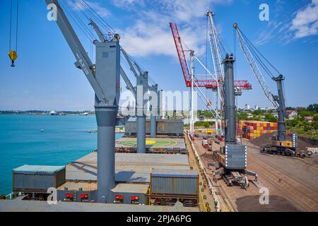 Betrieb mit Kohle im Seehafen. Kohle wird auf Massengutschiffe geladen. Kohleverladung durch Kräne auf Massengutschiffen Stockfoto