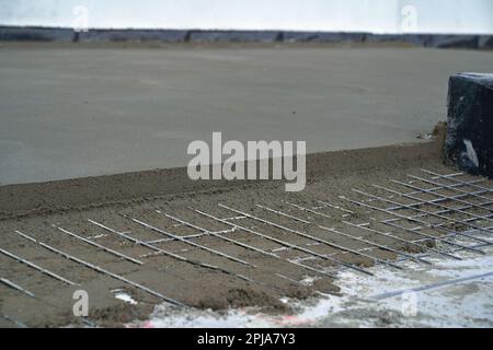 Installation von Zementbodenbodenbohlen mit Bewehrungsstahl. Maschinenboden-Einbaubohle. Stockfoto