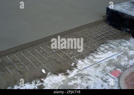 Installation von Zementbodenbodenbohlen mit Bewehrungsstahl. Maschinenboden-Einbaubohle. Stockfoto
