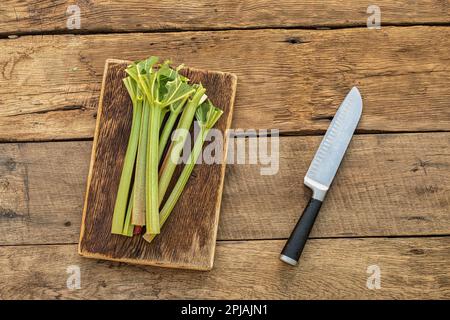 Frisch gepflückte Rhabarberstangen, in der Küche auf einem Schneidebrett, auf einem alten Holztisch. Fertig zum Kochen. Frische vegetarische Speisen. Stockfoto