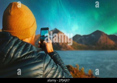 Mann mit Smartphone fotografiert Nordlichter Winterreisen in Norwegen Abenteuer Urlaub Outdoor Blogger Beeinflusser Lifestyle modern online tec Stockfoto