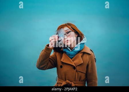 Porträt einer wunderschönen jungen, rothaarigen Asiatin, die ein durchsichtiges Stück Eis in der Hand hält und vor dem Hintergrund eines gefrorenen Meeres i steht Stockfoto