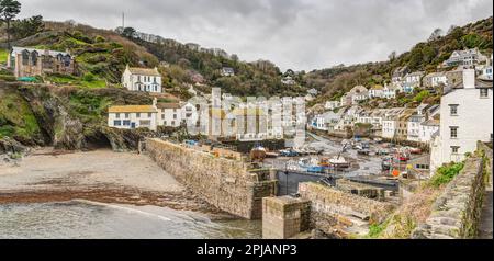 Ein Panoramablick auf den Hafen von Polperro voller festgelegter Boote, umgeben von dem Dorf und dem Strand bei Ebbe. Eine reizende Umgebung, die bei Tagesbesuchern sehr beliebt ist. Stockfoto