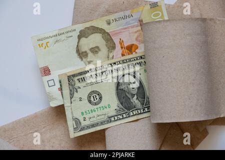 Ein amerikanischer Dollar und einhundert ukrainische Hrywna liegen auf Toilettenpapier auf einer Nahaufnahme mit weißem Hintergrund Stockfoto