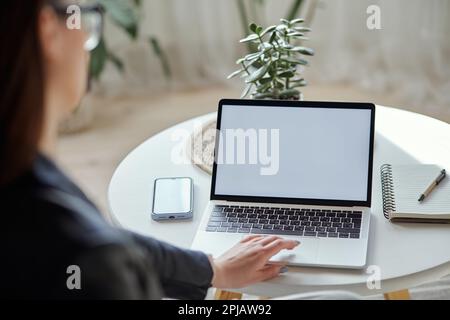 Modell eines weißen Laptops und einer Frau mit Handy, die zu Hause am Tisch sitzt, Rückansicht Stockfoto