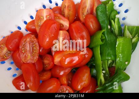 Geschnittene Kirschtomaten in Kombination mit Padrón-Paprika in einem weißen Sieb. Stockfoto