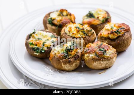 Gebackene Champignons, gefüllt mit Käse, Petersilie und geröstetem Knoblauch auf weißem Teller. Selektiver Fokus. Gesundes Lebensmittelkonzept Stockfoto