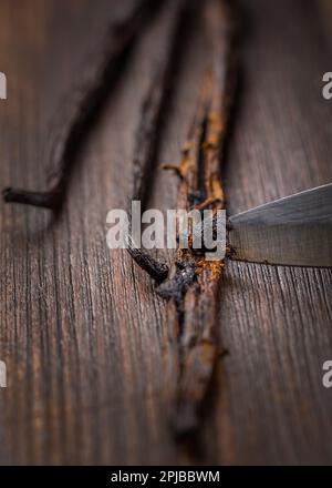 Vanillebohnen und Samenschoten mit Messer auf Holzhintergrund. Zubereitung von Vanille als Backzutat Stockfoto