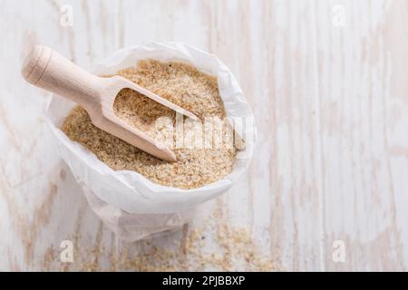 Psylliumhaufen (Plantago ovata) in einem kleinen Sack auf einem Holztisch. Psylliumschalen, auch Isabgol genannt, sind Fasern, die aus den Samen der Pflanze gewonnen werden Stockfoto