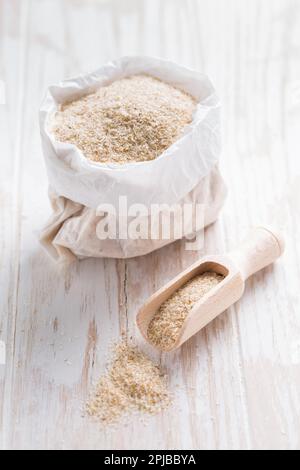 Psylliumhaufen (Plantago ovata) in einem kleinen Sack auf einem Holztisch. Psylliumschalen, auch Isabgol genannt, sind Fasern, die aus den Samen der Pflanze gewonnen werden Stockfoto