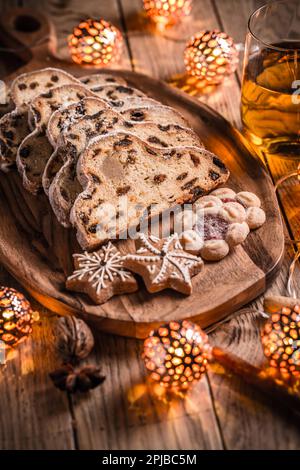 Weihnachtsstollen und Kekse mit Apfelwein und Weihnachtsbeleuchtung. Traditioneller Süßobstlaaf mit Puderzucker Stockfoto