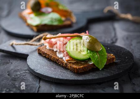 Offenes Sandwich mit Prosciutto auf schwarzem Brot (Pumpernickel) auf Schneidebrett Stockfoto