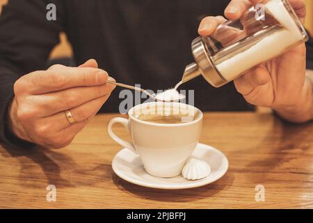 Nahaufnahme der Hand eines Geschäftsmannes mit Kaffee in einem Café, Gießen Sie Zucker in den Löffel, in eine Tasse Espresso, Morgenkaffee-Konzept. Kaffeebremse. Guten Morgen Stockfoto