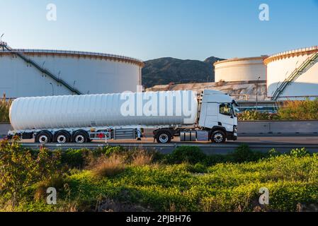 Zisternwagen für den Transport kryogener gefährlicher Gase, die auf einer Straße mit großen Ablagerungen einer Raffinerie zirkulieren. Stockfoto