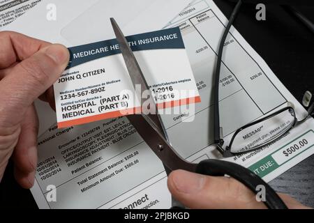 Selektive Fokussierung des Menschen schneidet eine gefälschte Medicare-Schnitt mit gefälschter Krankenhausrechnung im Hintergrund. Konzept der hohen Kosten der medizinischen Versorgung. Stockfoto