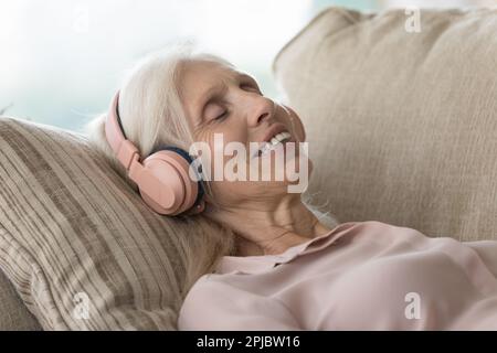 Glückliche, entspannte Rentnerin mit Kopfhörern, die Musik hört Stockfoto