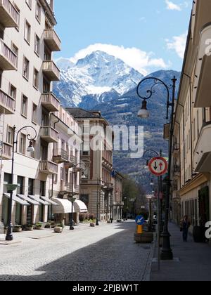 Aosta Street mit Straßenschildern und Hochhäusern an einem sonnigen Tag, mit schneebedeckten Bergen in den alpen dahinter. Aosta-Tal, Italien Stockfoto