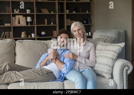 Glückliche ältere Mutter, die einen hübschen jungen erwachsenen Sohn umarmt Stockfoto