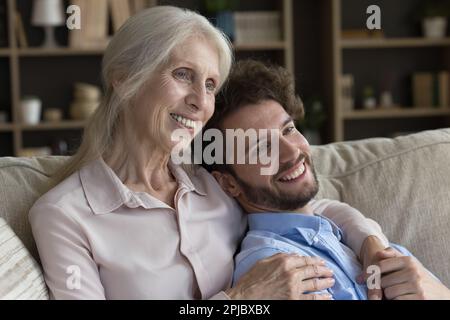 Fröhliche ältere Oma, die einen gut aussehenden erwachsenen Enkelkinder umarmt Stockfoto