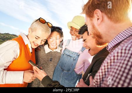 Viele Lachen über multirassische Freunde, die ihr Handy benutzen. Menschen, die mit sozialen Medien unterhalten werden. Stockfoto