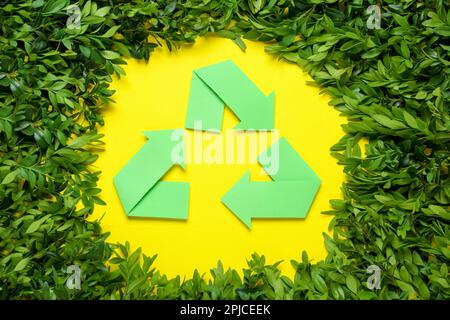 Recycling-Symbol und Zweige der grünen Pflanze auf gelbem Hintergrund, flach verlegt Stockfoto