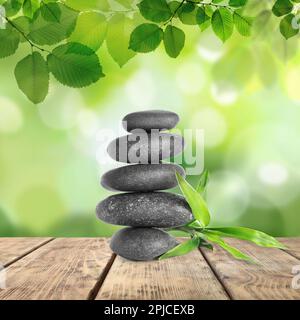 Gestapelte Steine und Bambusstämme auf einem Holztisch unter grünen Blättern vor verschwommenem Hintergrund. Zen-Konzept Stockfoto