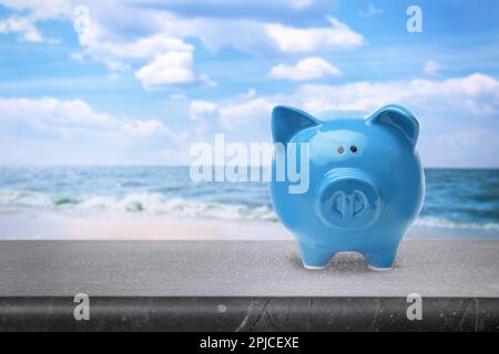 Sparen Geld für den Sommerurlaub. Sparschwein auf einer Steinfläche nahe dem Meer, Platz für Text Stockfoto