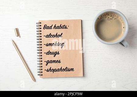 Notizbuch mit Liste der schlechten Gewohnheiten und Tasse Kaffee auf weißem Holztisch, flach liegend Stockfoto