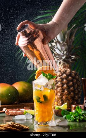 Sommercocktail mit Wodka, Ananassaft, Mango, Eis. Longdrink oder kalter Mocktail. Der Barkeeper schüttelt den Kupferschüttler mit Spritzern, eingefrorener Bewegung und Stockfoto