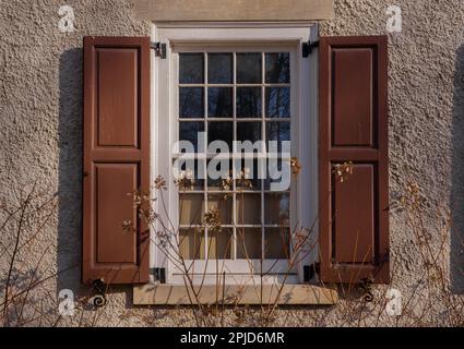 Fenster mit Holzläden und Blumen vor einer Steinmauer. Architekturdetails Stockfoto