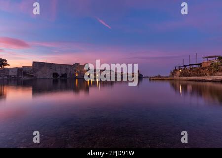 Königliche Burg von Collioure über dem stillen Wasser (Meer) in Coullioure, Frankreich nach dem Sonnenuntergang. Pink- und Violetttöne, der Himmel reflektiert sich im Wasser Stockfoto