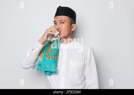 Lächelnder junger asiatischer Mann in einem muslimischen Hemd, der traditionelle Begrüßungen auf weißem Hintergrund trägt. Stockfoto