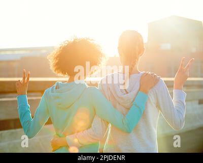 Was für ein glorreicher Morgen. Rückansicht von zwei Joggingweibchen, die beim Sonnenaufgang Friedenszeichen machten. Stockfoto
