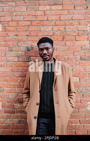 Ein afroamerikanischer Mann, der in die Kamera schaut, während er gegen eine Mauer steht. Stockfoto