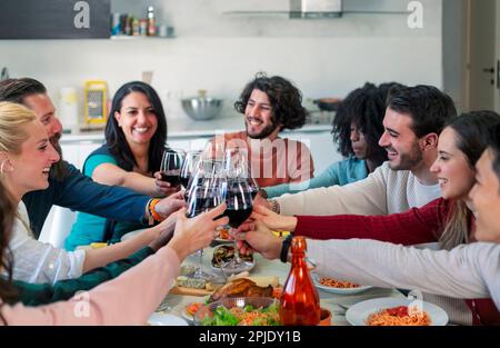 Junge Leute halten Weingläser und toasten, während sie gemeinsam am Tisch während der Dinnerparty feiern Stockfoto