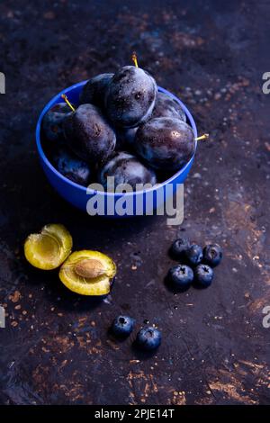 Reife, saftige Pflaumen und Blaubeeren in einer Schüssel auf einem Tisch. Sommerfrüchte. Stockfoto