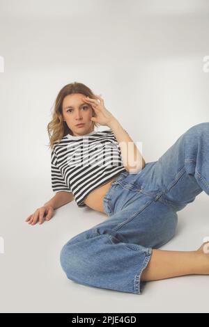 Modeporträt einer jungen Frau in lässigen weiten Jeans und gestreiftem T-Shirt auf weißem Hintergrund Stockfoto