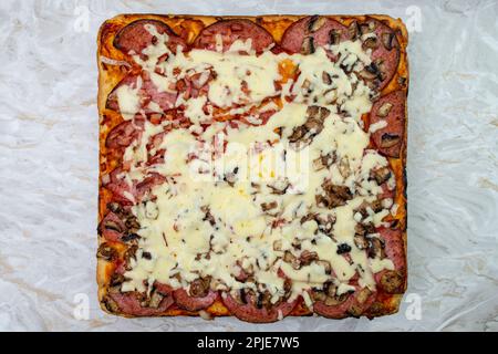 Quadratische Pizza mit Käse und Salami auf weißem Marmorhintergrund, flache Nahaufnahme Stockfoto