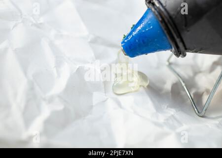 Heißklebepistole mit Silikonspritzer auf zerknittertem Papier, Nahaufnahme mit weichem Fokus Stockfoto