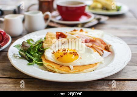 Leckeres Frühstück mit Pfannkuchen, Spiegeleiern und Speck auf dem Tisch. Stockfoto