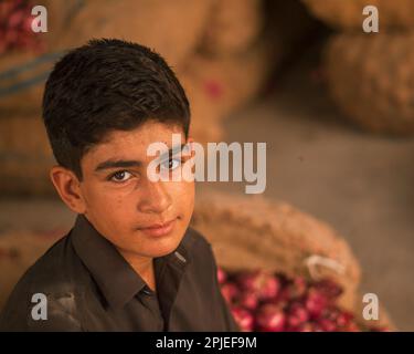 Karatschi Pakistan 2019, ein Junge sitzt auf dem Gemüsemarkt und arrangiert Zwiebeln am frühen Morgen im Sabzi Mandi. Stockfoto