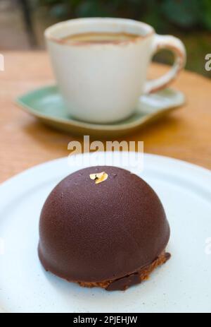 Nahaufnahme von Schokoladen-Mousse-Kuppelkuchen mit verschwommener Kaffeetasse im Hintergrund Stockfoto