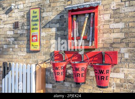 Feuereimer und Ausrüstung sowie eine alte Raucherwerbung an der Arley Station der Severn Valley Steam Railway, Worcestershire, England Stockfoto