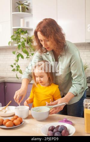 Großmutter und Enkelin bereiten Kuchenteig zu, verbringen Zeit miteinander, Familienbeziehungen, Liebe. Hilft Stockfoto