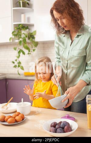 Großmutter und Enkelin bereiten Kuchenteig zu, verbringen Zeit miteinander, Familienbeziehungen, Liebe. Komisch Stockfoto