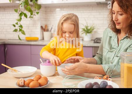 Großmutter und Enkelin bereiten Kuchenteig zu, verbringen Zeit miteinander, Familienbeziehungen, Liebe. Zerbrechen Sie das Ei Stockfoto