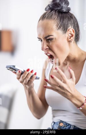 Wütende Frau schreit ins Telefon, das sie an einem Lautsprecher in der Hand hält. Stockfoto