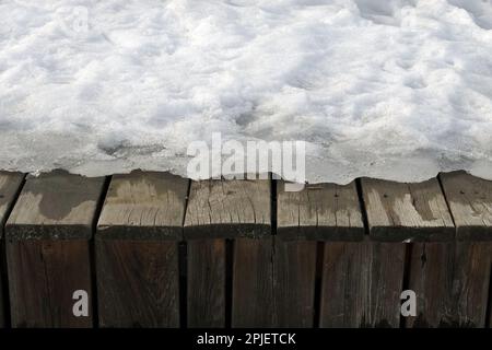 Schmelzen im Frühlingsschnee auf der Oberfläche der alten braunen Holzbretter im Freien Vorderansicht Nahaufnahme Stockfoto